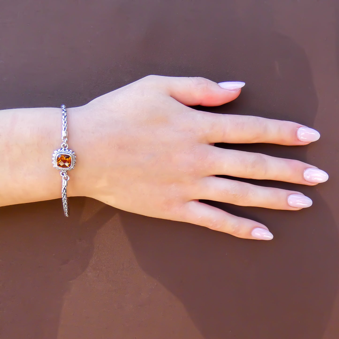 Woman wearing a silver bracelet with wheat chain arms and a square citrine gemstone in the center.