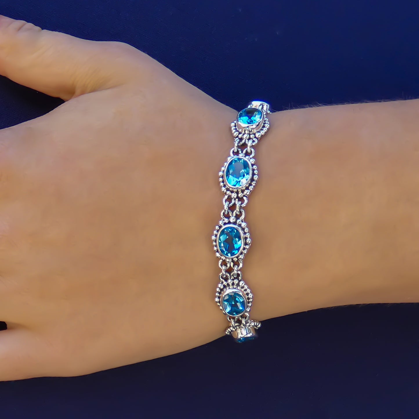 Woman wearing a silver bracelet with oval blue topaz gemstones and beaded accents.