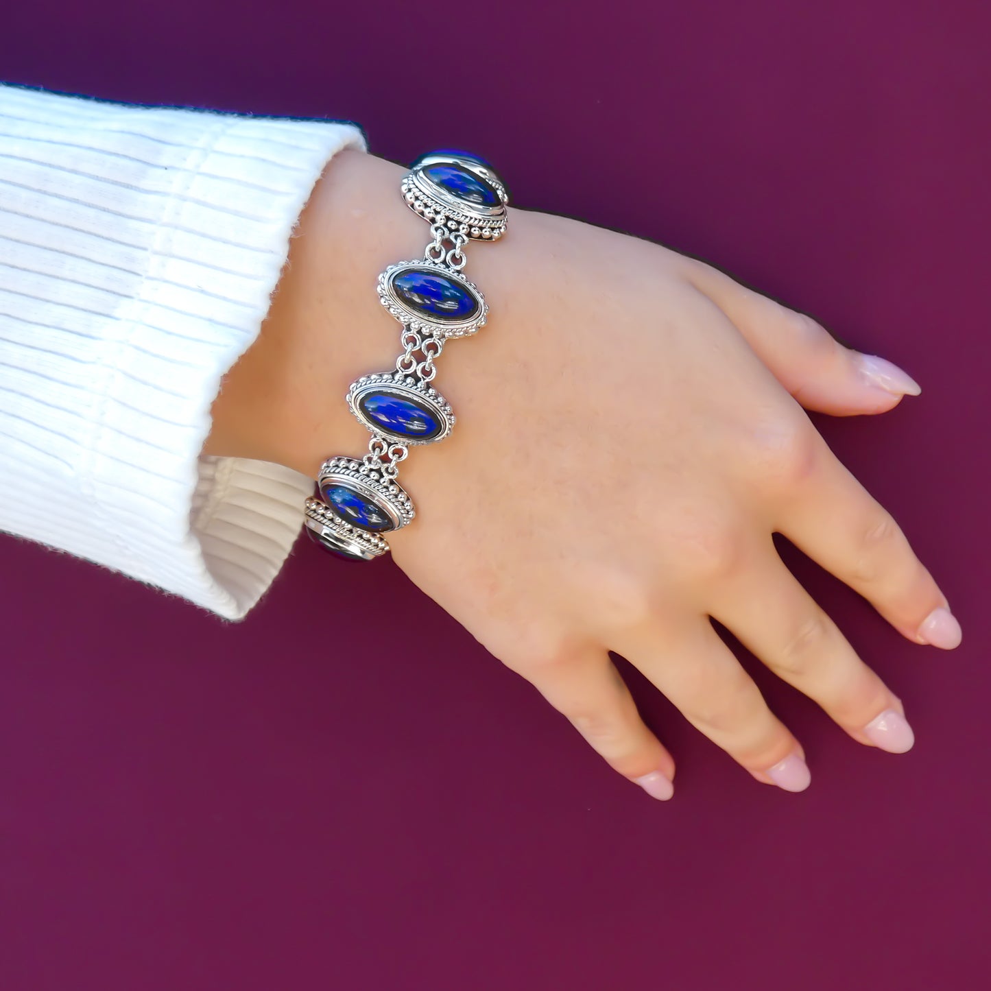 Woman wearing a silver link bracelet with oval lapis stones.