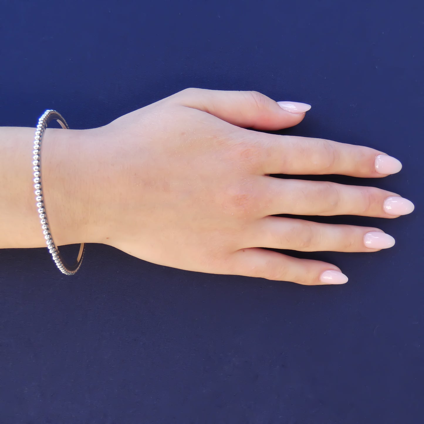 Woman wearing a silver bangle bracelet with a hammered center and beaded edge.
