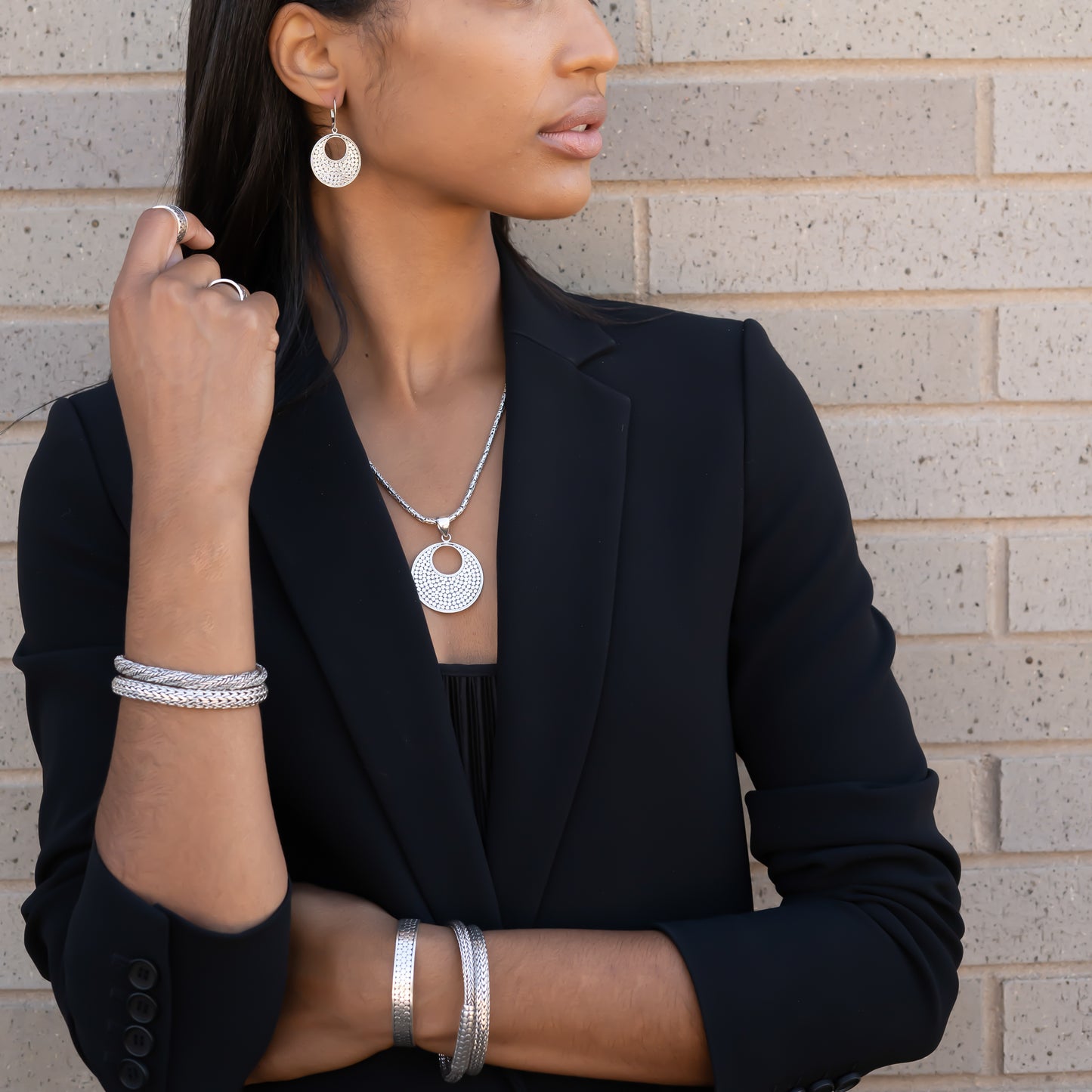 Woman wearing five silver bracelets, silver earrings, a silver chain and pendant.
