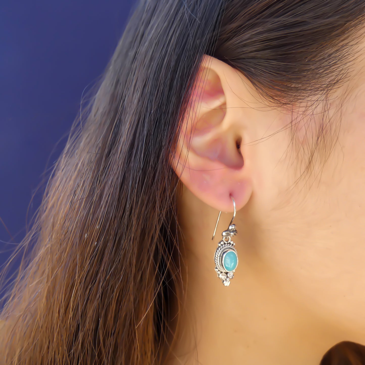 Woman wearing silver floral earrings with oval amazonite gemstones.