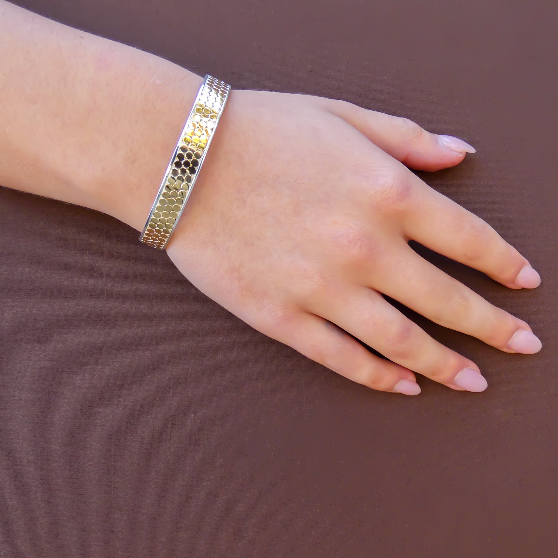 Woman wearing a silver and gold cuff bracelet with three rows of flat dots.