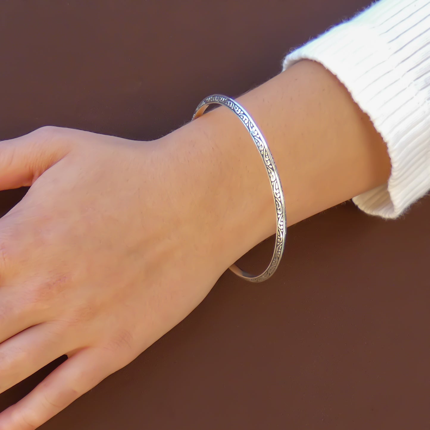 Woman wearing a silver bangle bracelet with carved filigree designs.