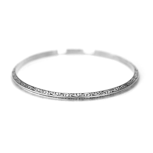Silver bangle bracelet with carved filigree designs and a triangular profile.