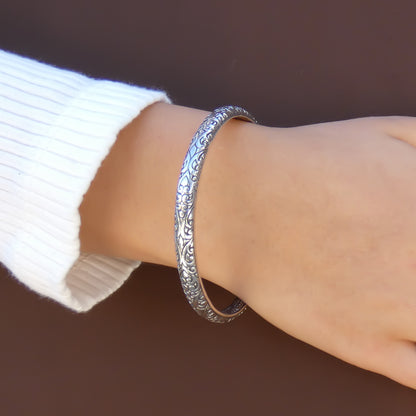 Woman wearing a thick silver bangle bracelet with carved filigree designs.