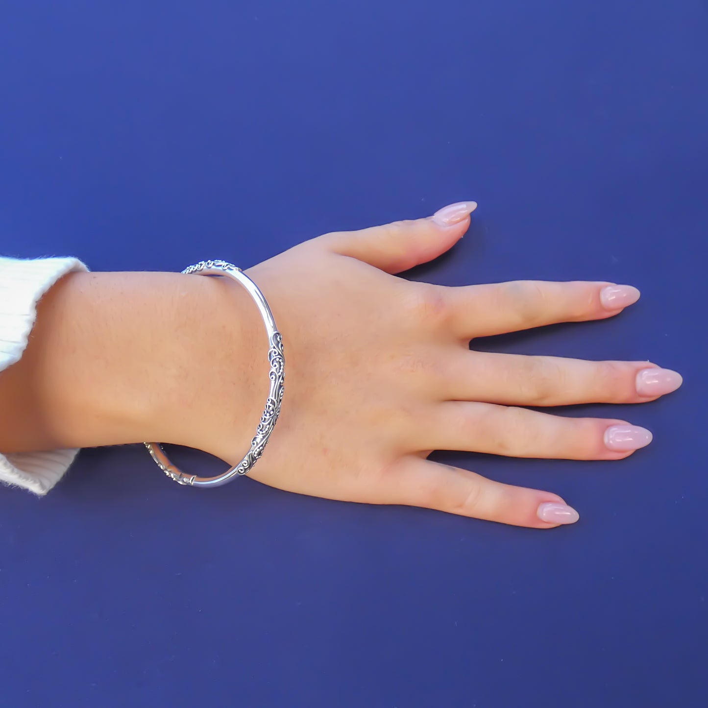 Woman wearing a silver bangle bracelet with three areas of filigree wire design adornment.