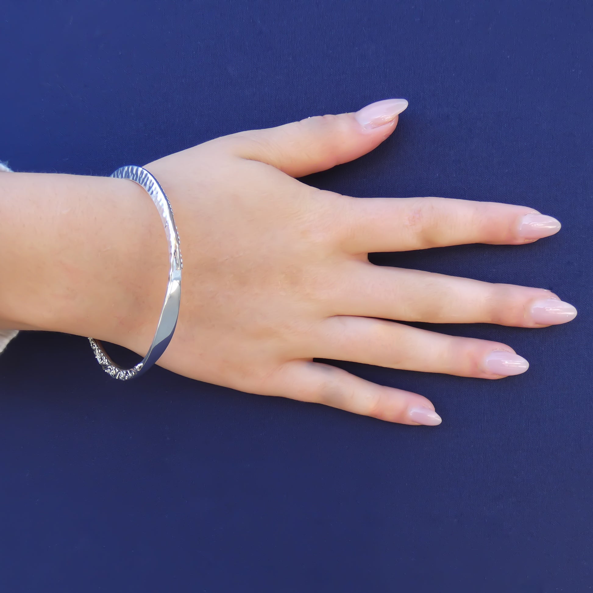 Woman wearing a silver bangle bracelet with hammered and filigree design elements.