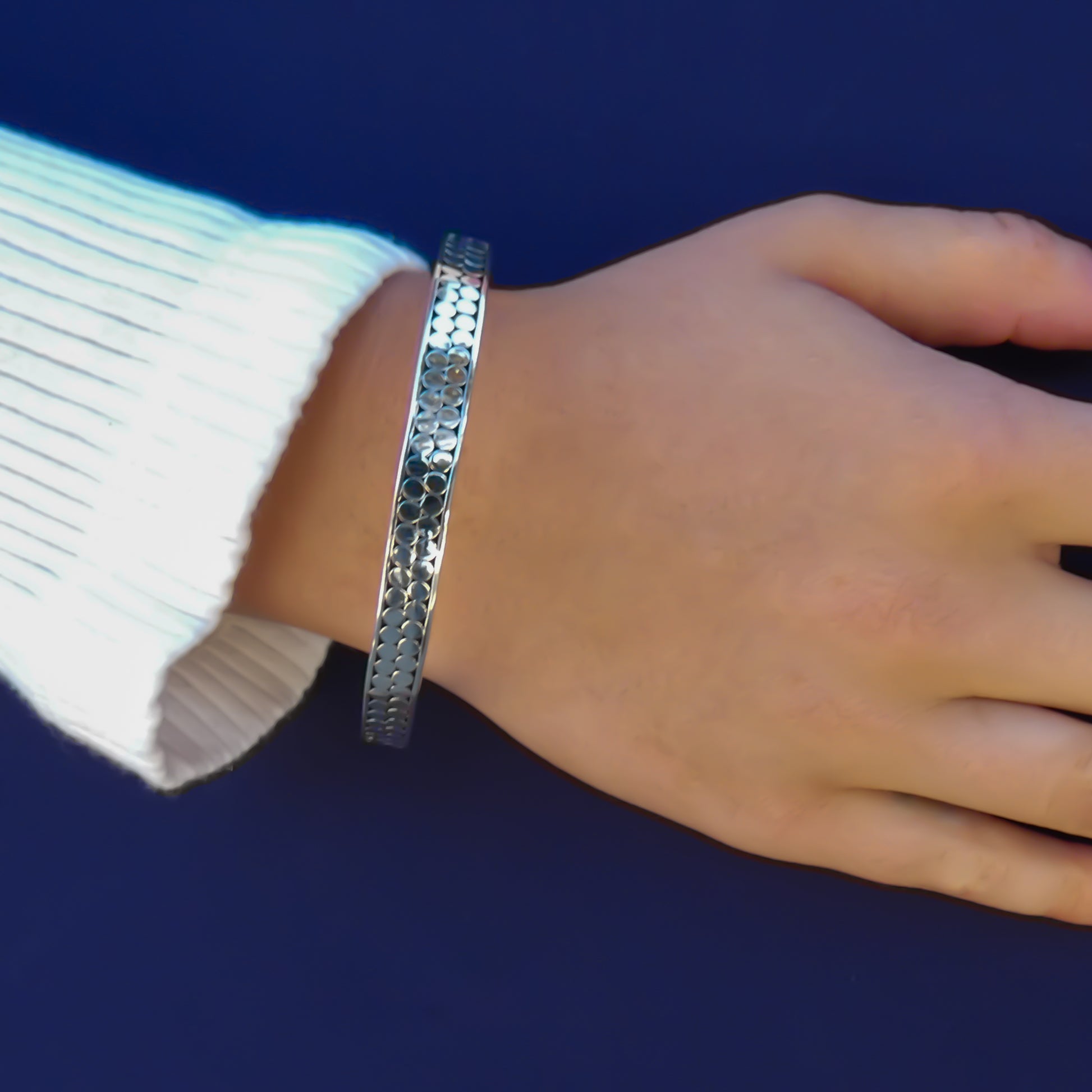 Woman wearing a silver bangle bracelet with two rows of flat silver dots.