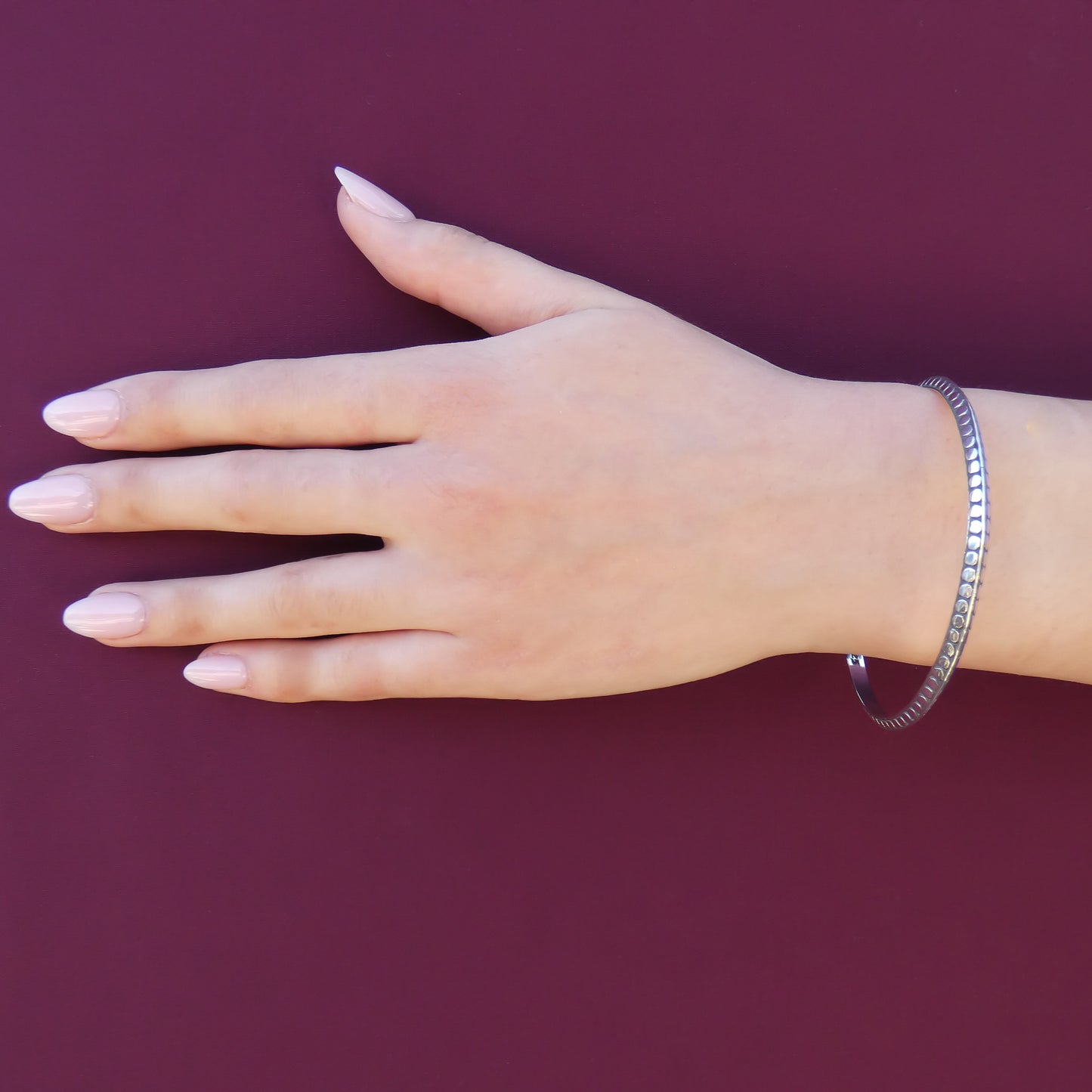 Woman wearing a silver bangle bracelet with flat dot design and a triangular profile.