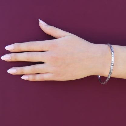 Woman wearing a silver bangle bracelet with flat dot design and a triangular profile.