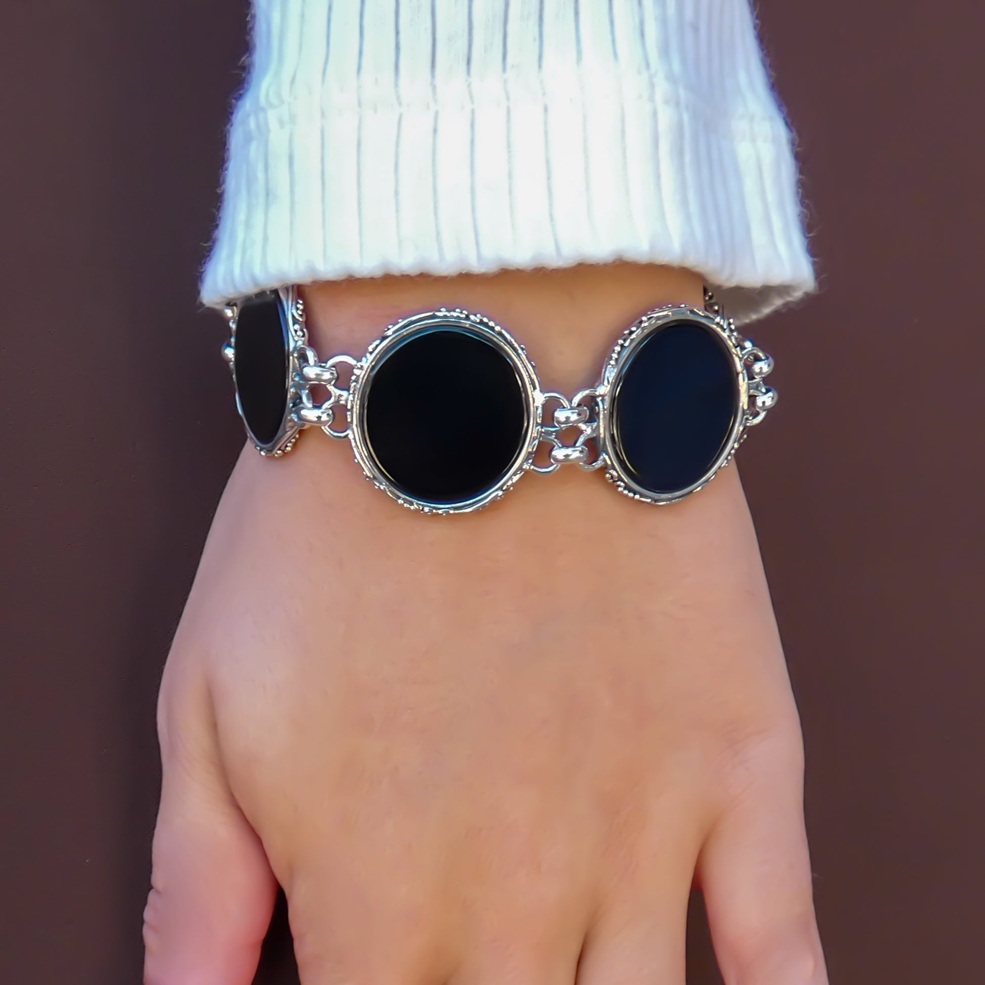 Woman wearing a bracelet made of round onyx discs with silver borders.