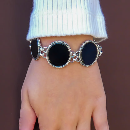 Woman wearing a bracelet made of round onyx discs with silver borders.