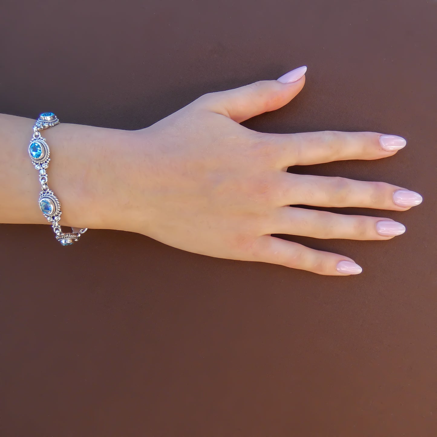 Woman wearing silver and blue topaz link bracelet.