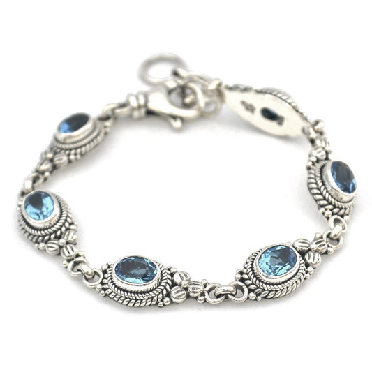 Silver bracelet with six links holding blue topaz stones and floral accents.