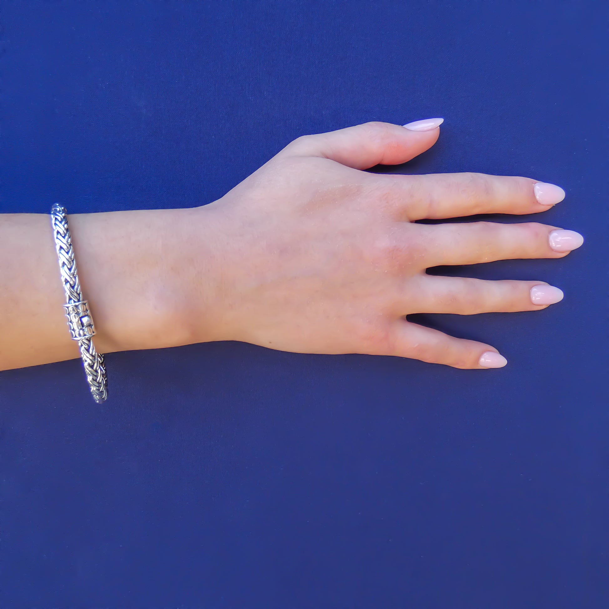 Woman wearing a thick silver wheat chain bracelet with a single button barrel clasp.