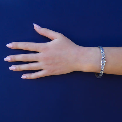 Woman wearing a silver snake chain bracelet with a single button barrel clasp.