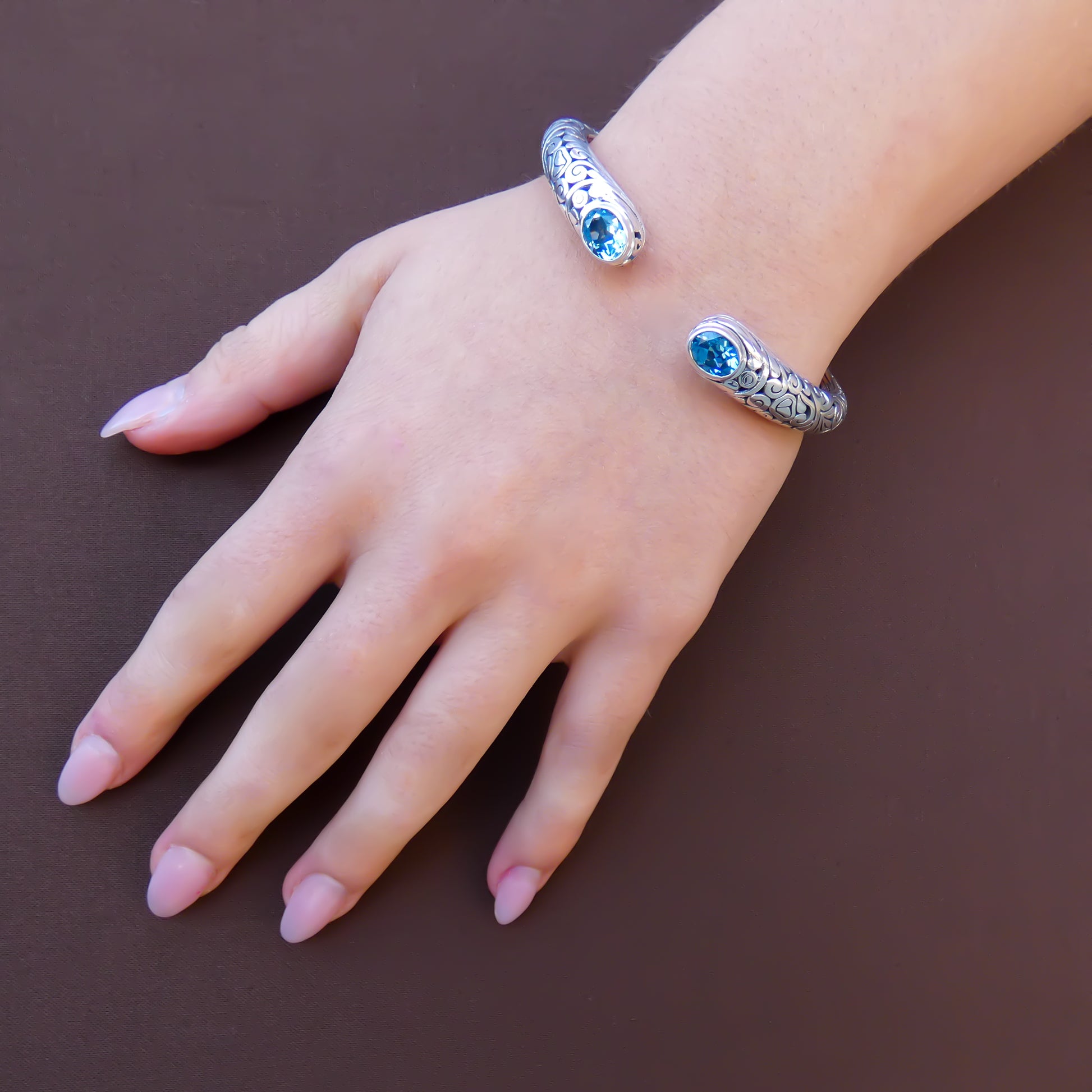 Woman wearing a hinged silver cuff bracelet with carved filigree design and two blue topaz gemstones.