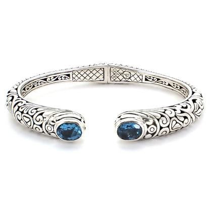 Hinged silver cuff bracelet with carved filigree design and two Swiss blue topaz gemstones.