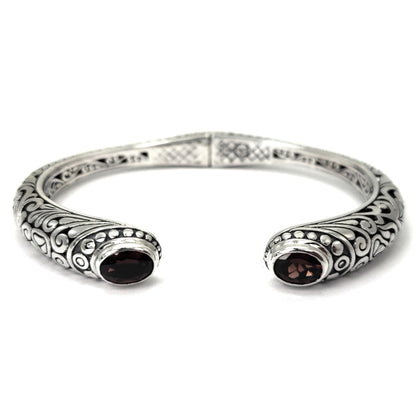 Hinged silver cuff bracelet with carved filigree design and two faceted garnet gemstones.