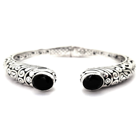 Hinged silver cuff bracelet with carved filigree design and two black onyx gemstones.