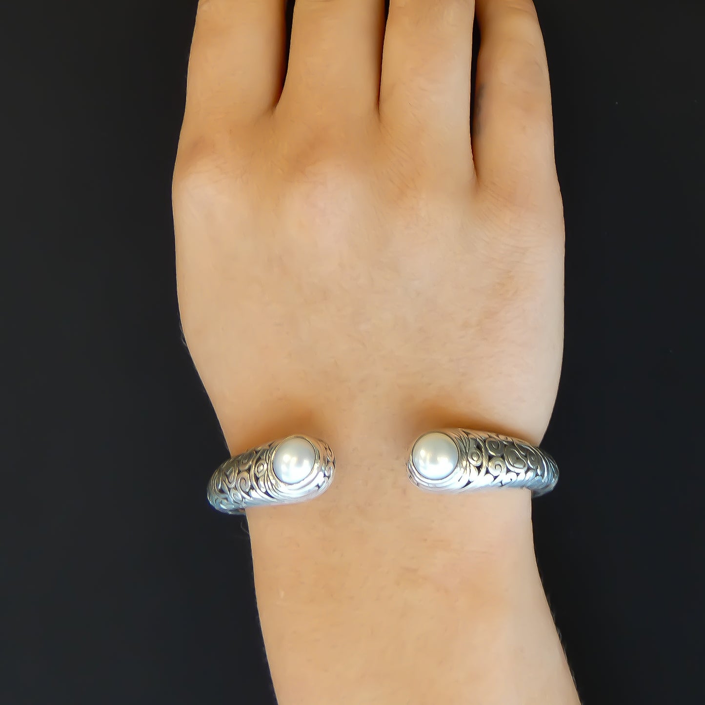 Woman wearing Hinged silver cuff bracelet with carved filigree design and two pearls.