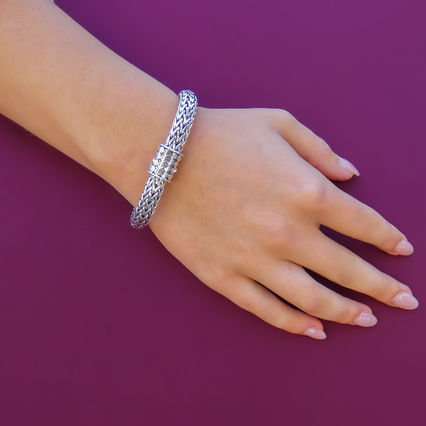 Woman wearing a silver snake chain bracelet with a two button barrel clasp.
