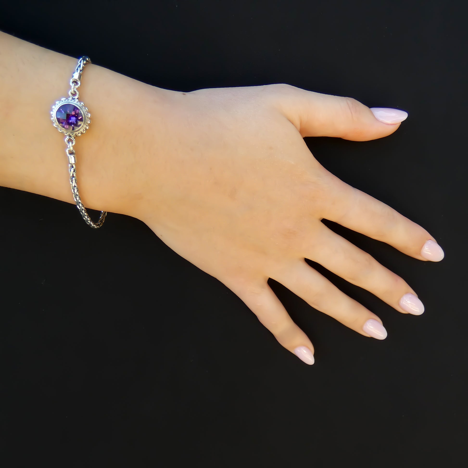 Woman wearing a silver bracelet with wheat chain arms and a single round purple amethyst gemstone in the middle.