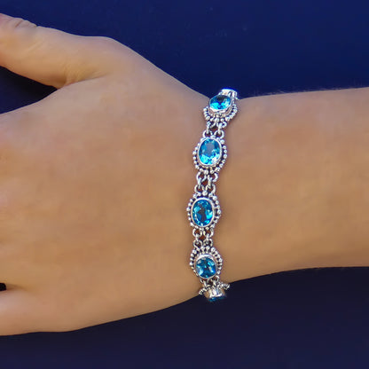 Woman wearing a silver bracelet with oval blue topaz gemstones and beaded accents.
