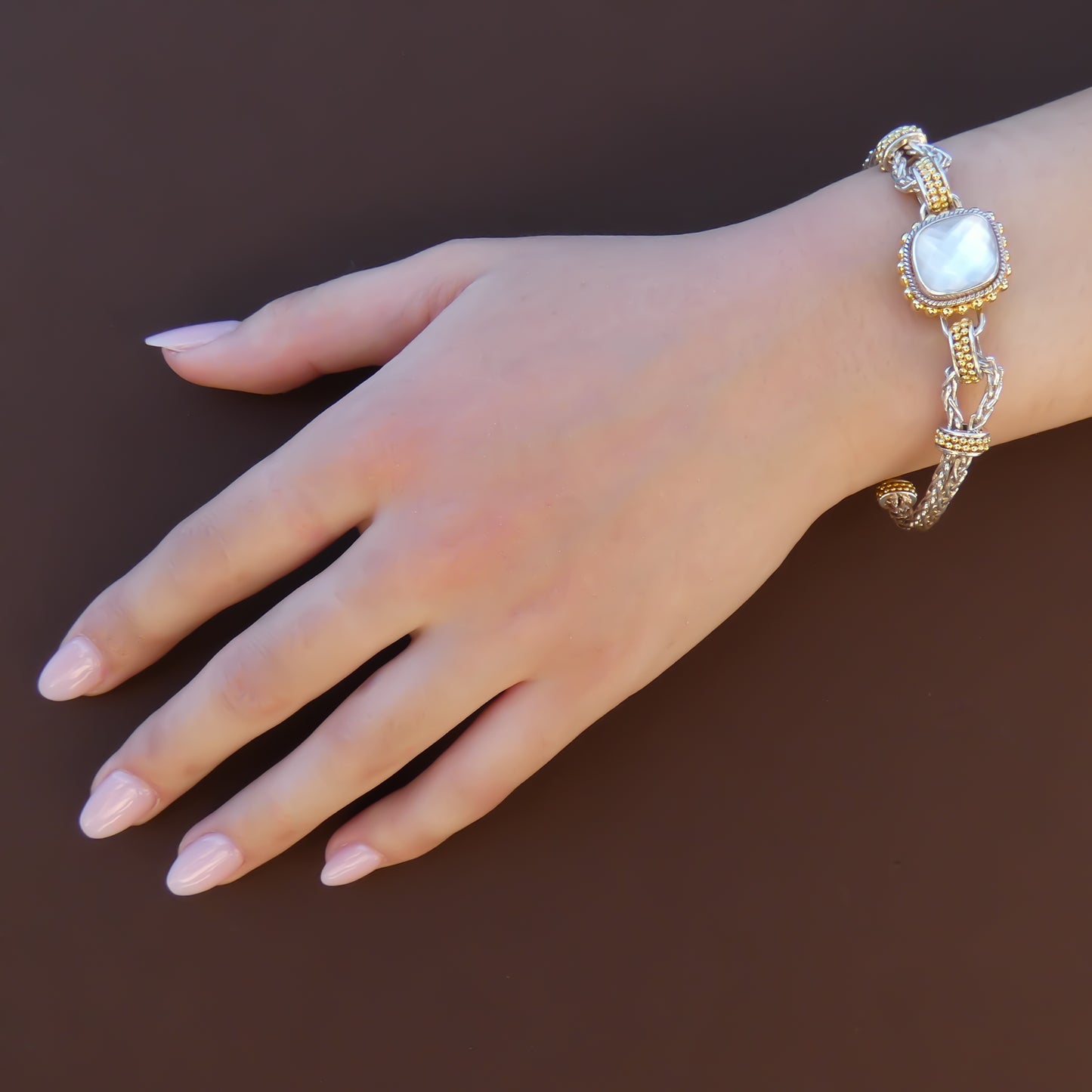 Woman wearing a silver and gold bracelet with a single central station that has a mother of pearl doublet.