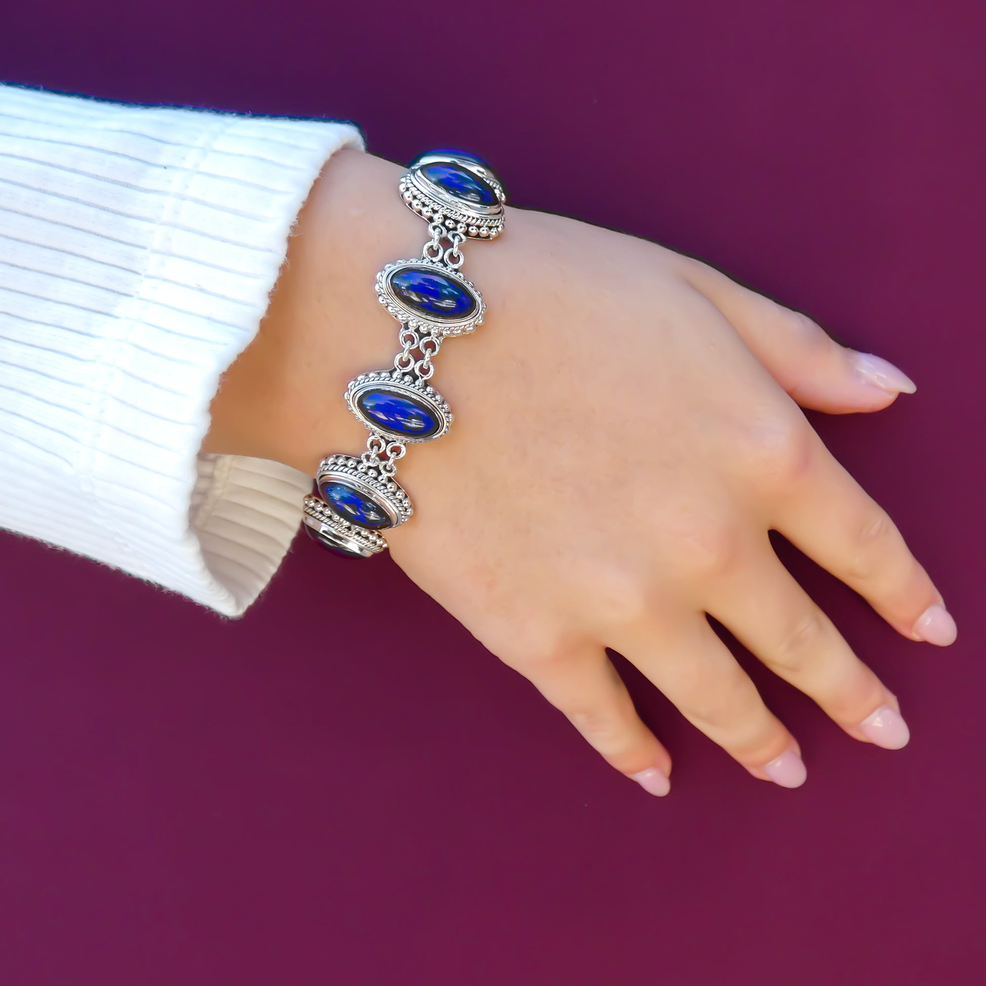 Woman wearing a silver link bracelet with oval lapis stones. 
