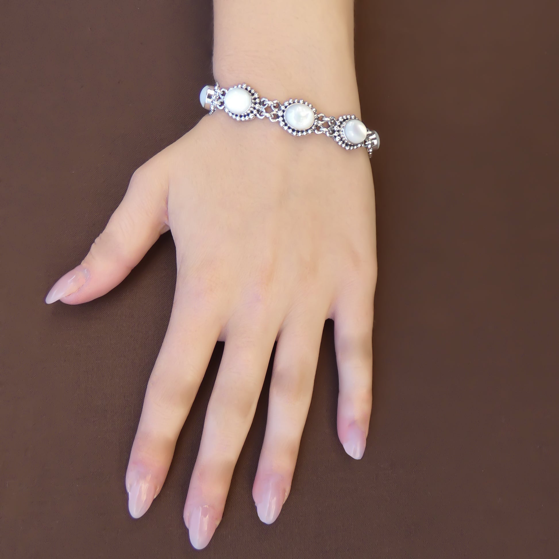 Woman wearing a silver link bracelet with oval mother of pearl stones and bead accents.