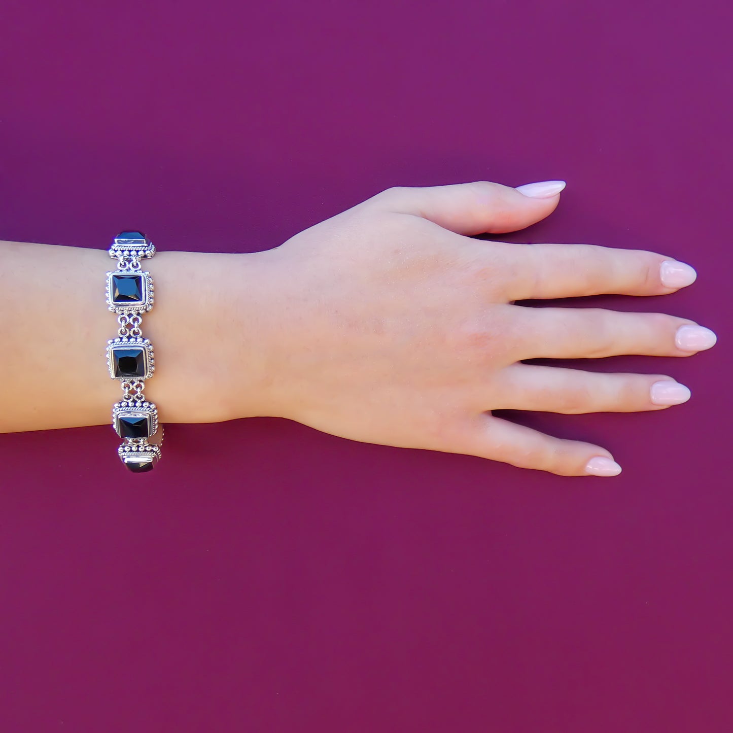 Woman wearing a silver link bracelet with square faceted onyx gemstones