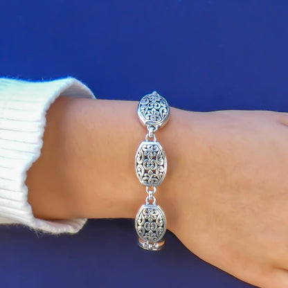 Woman wearing a silver bracelet with ornate oval links.