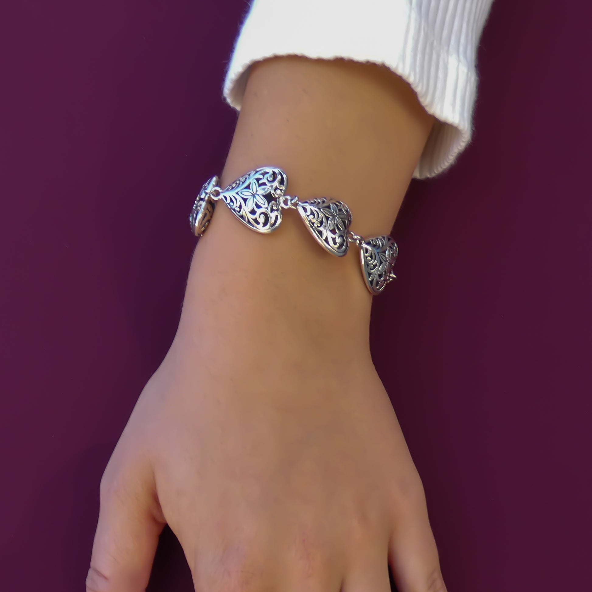 Woman wearing an ornate silver heart link bracelet.