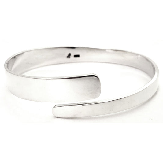 Silver bangle bracelet with a wide flat bypass design.