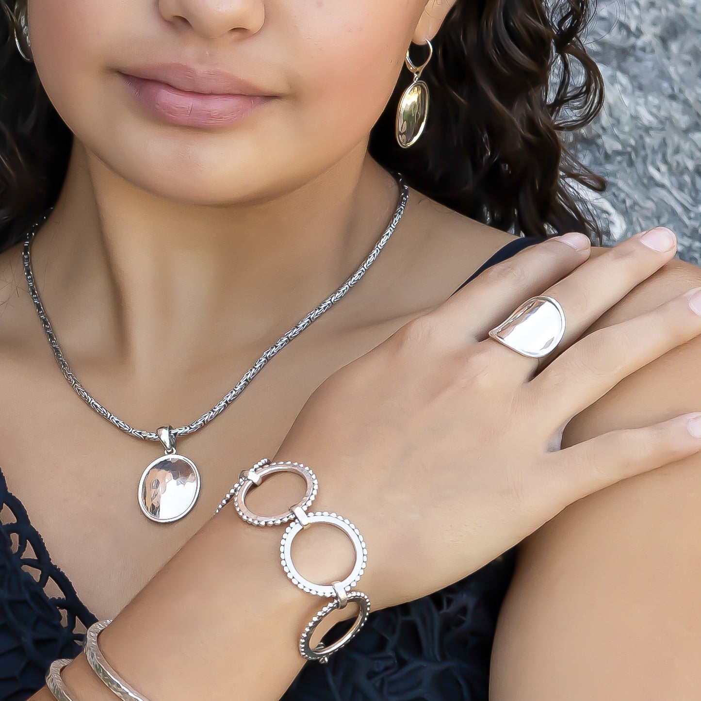 Woman wearing hammered oval ring, pendant, earrings, and ring link bracelet.