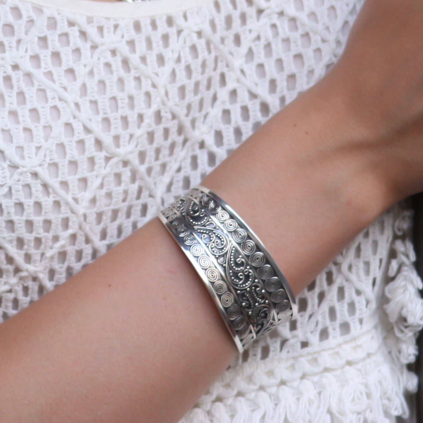 Woman wearing a silver cuff with lots of detailed silverwork.