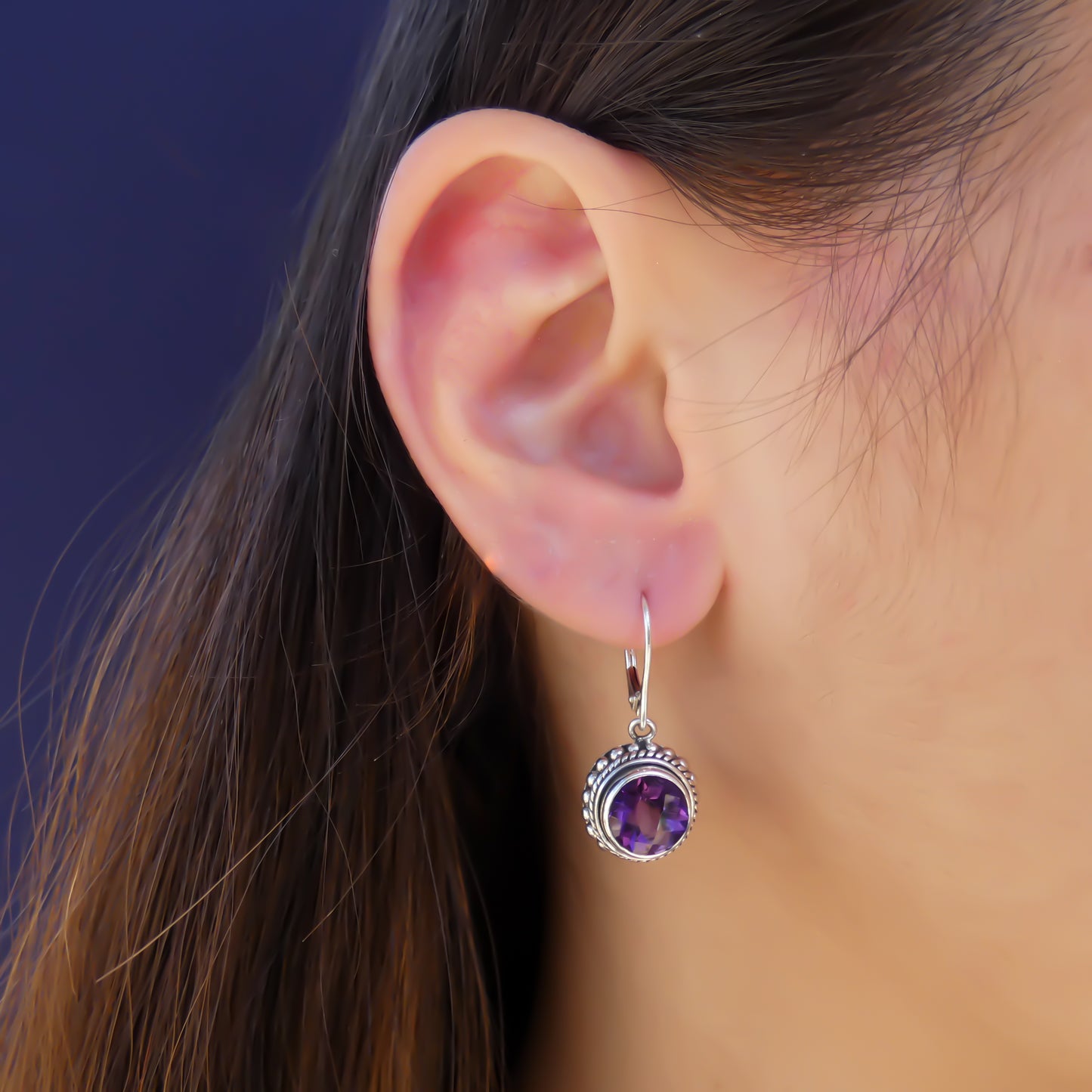 Woman wearing silver earrings with round purple amethyst gemstones.