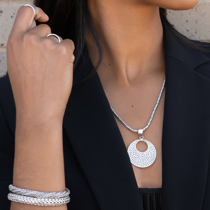 Woman wearing two silver snake chain bracelets and a silver round pendant.