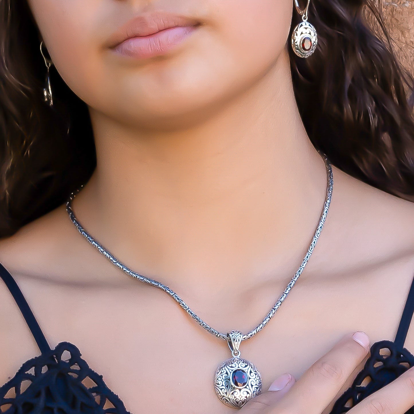 Woman wearing a byzantine chain necklace, silver and garnet pendant, and silver and garnet earrings.
