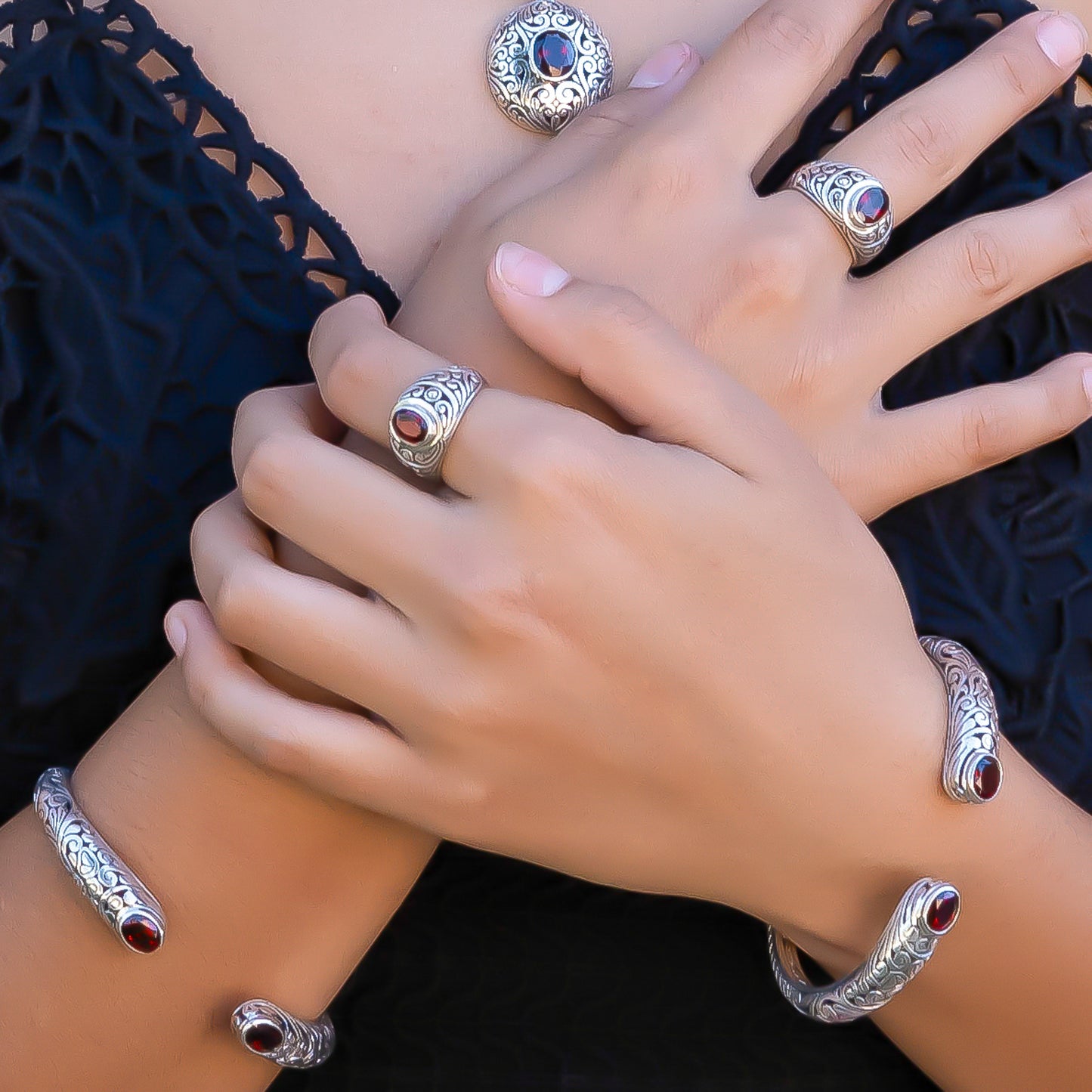 Woman wearing a variety of silver jewelry with faceted garnets and carved silver design elements.