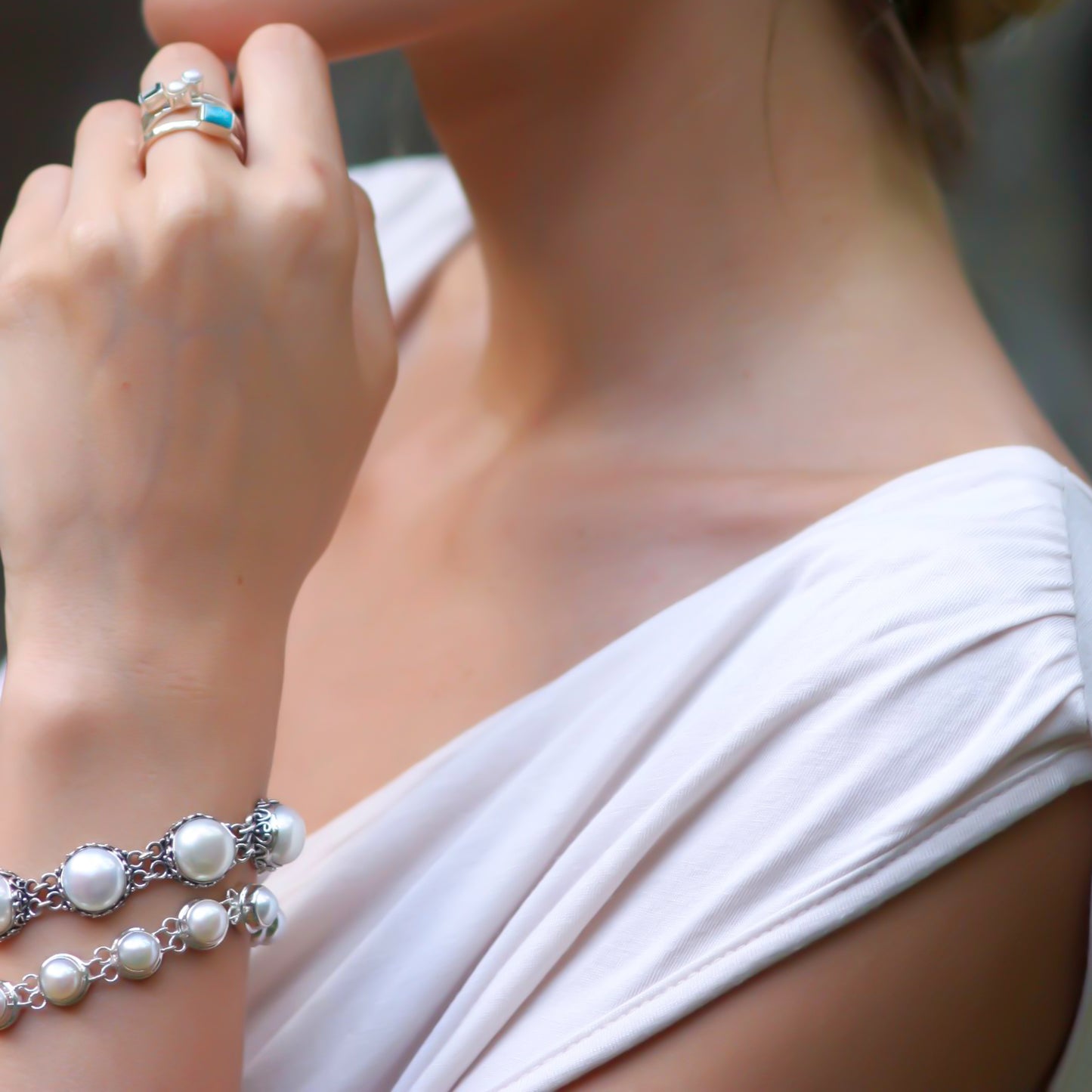 Close up of a woman wearing pearl bracelets and pearl and turquoise rings.