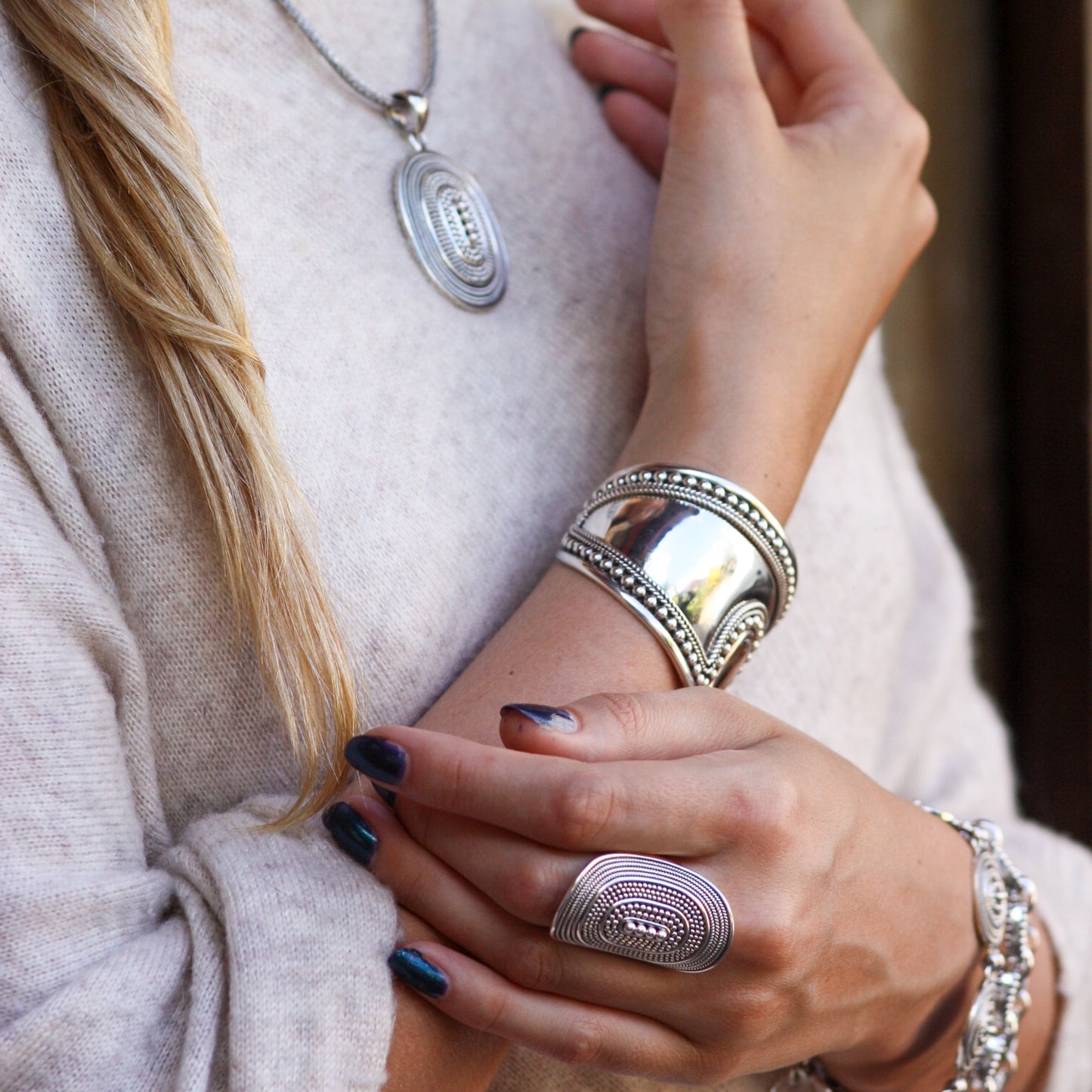 Woman wearing a beaded oval silver cuff bracelet, ring and pendant.