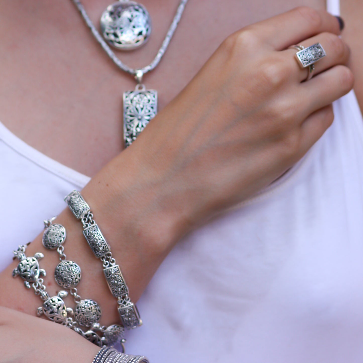 Woman wearing various silver bracelets, pendants and a ring.