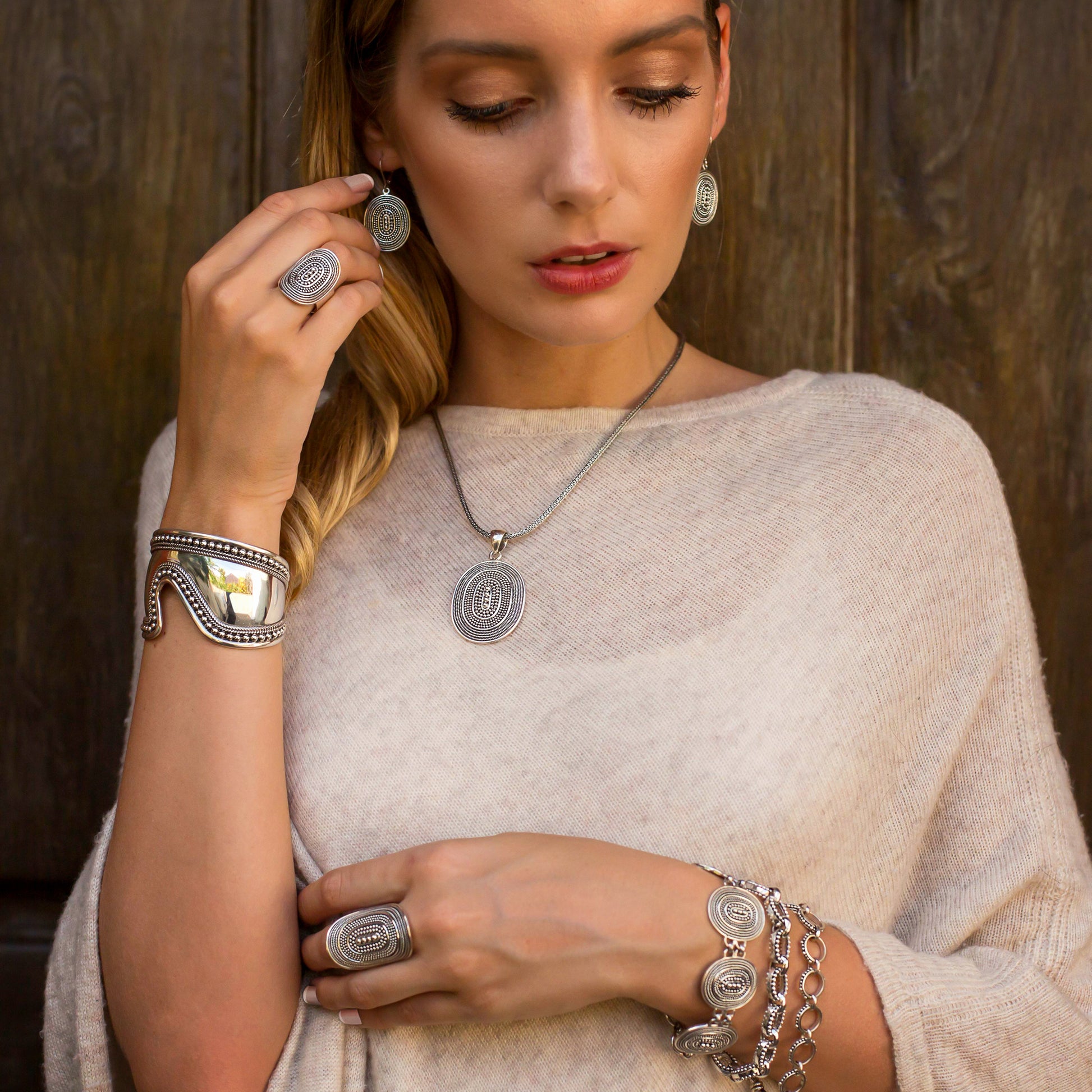 Woman wearing four silver bracelets, two silver rings, silver earrings and a silver pendant.