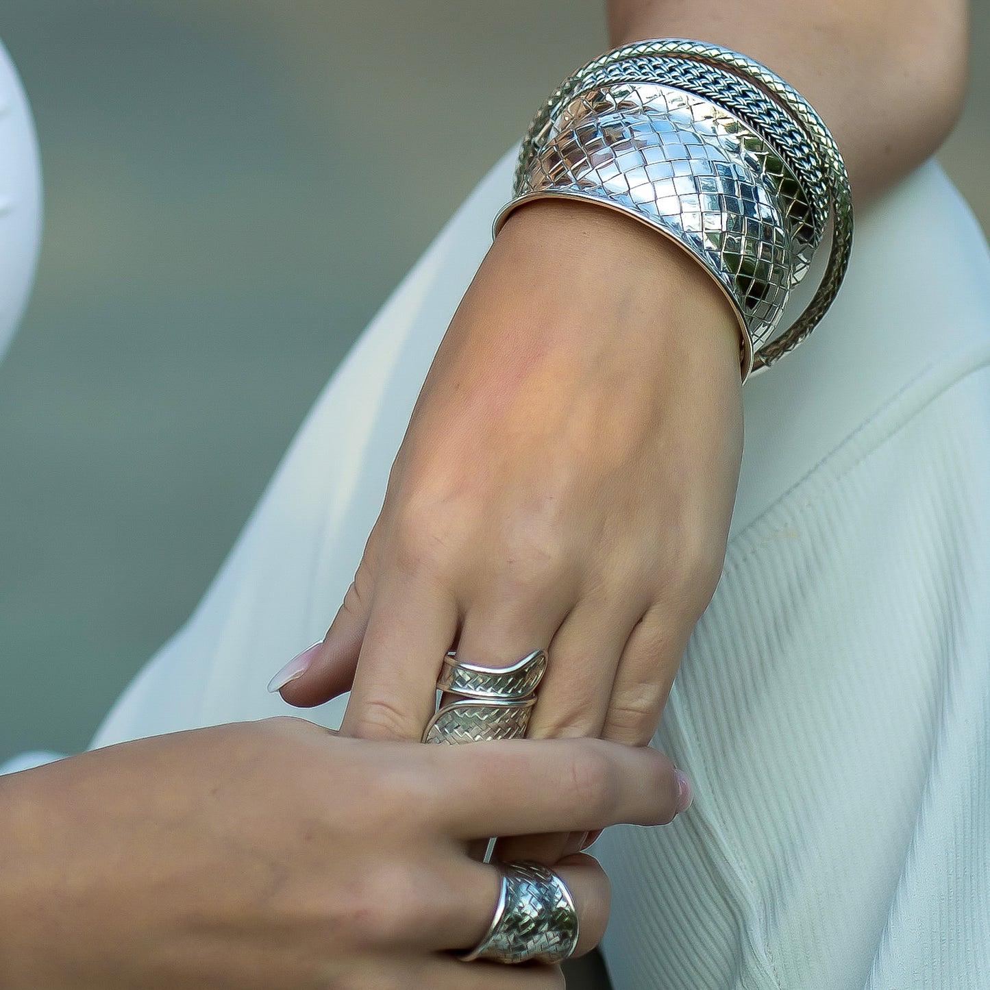 Woman wearing woven silver bracelets and woven silver rings.