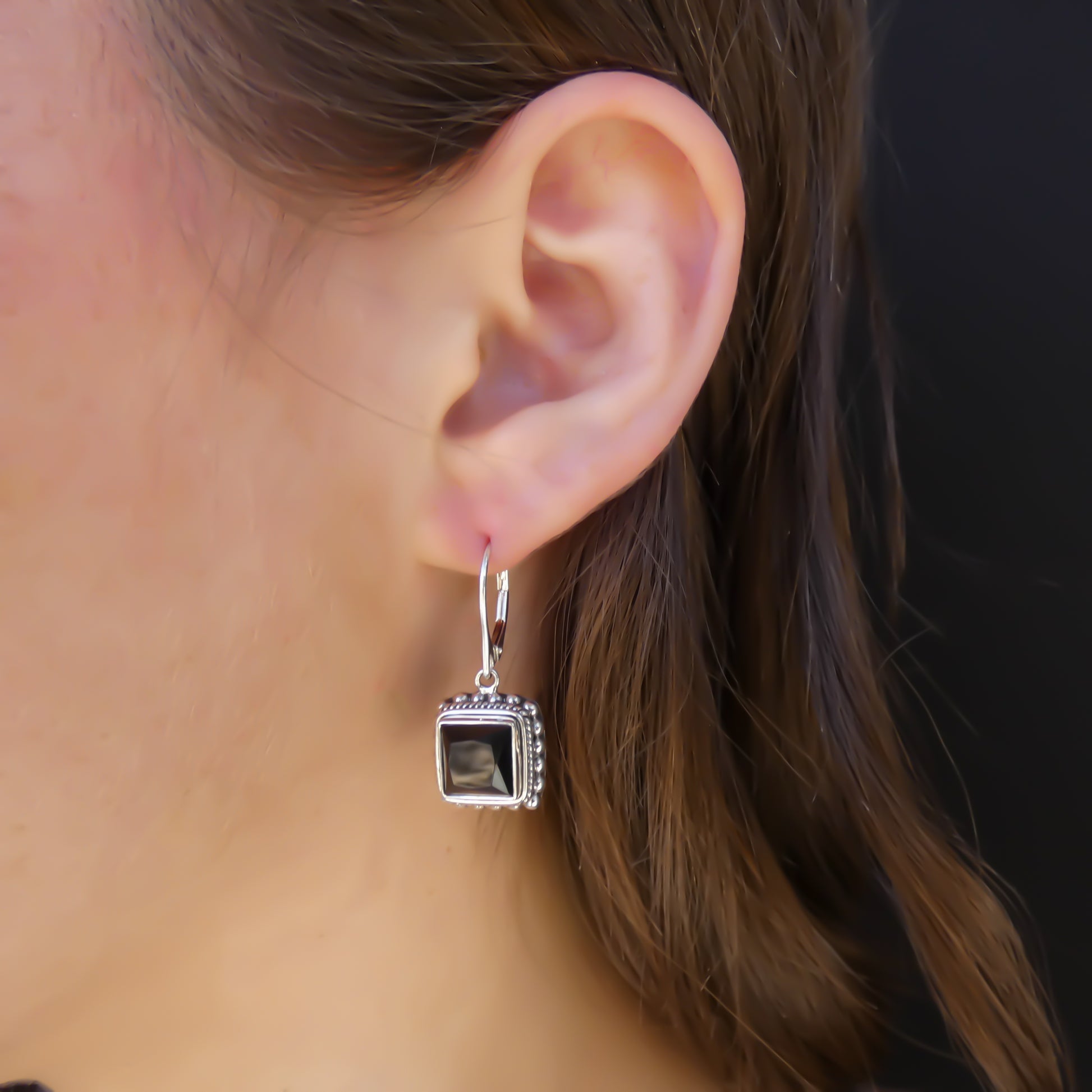 Woman wearing silver earrings with square onyx gemstones and beaded border.