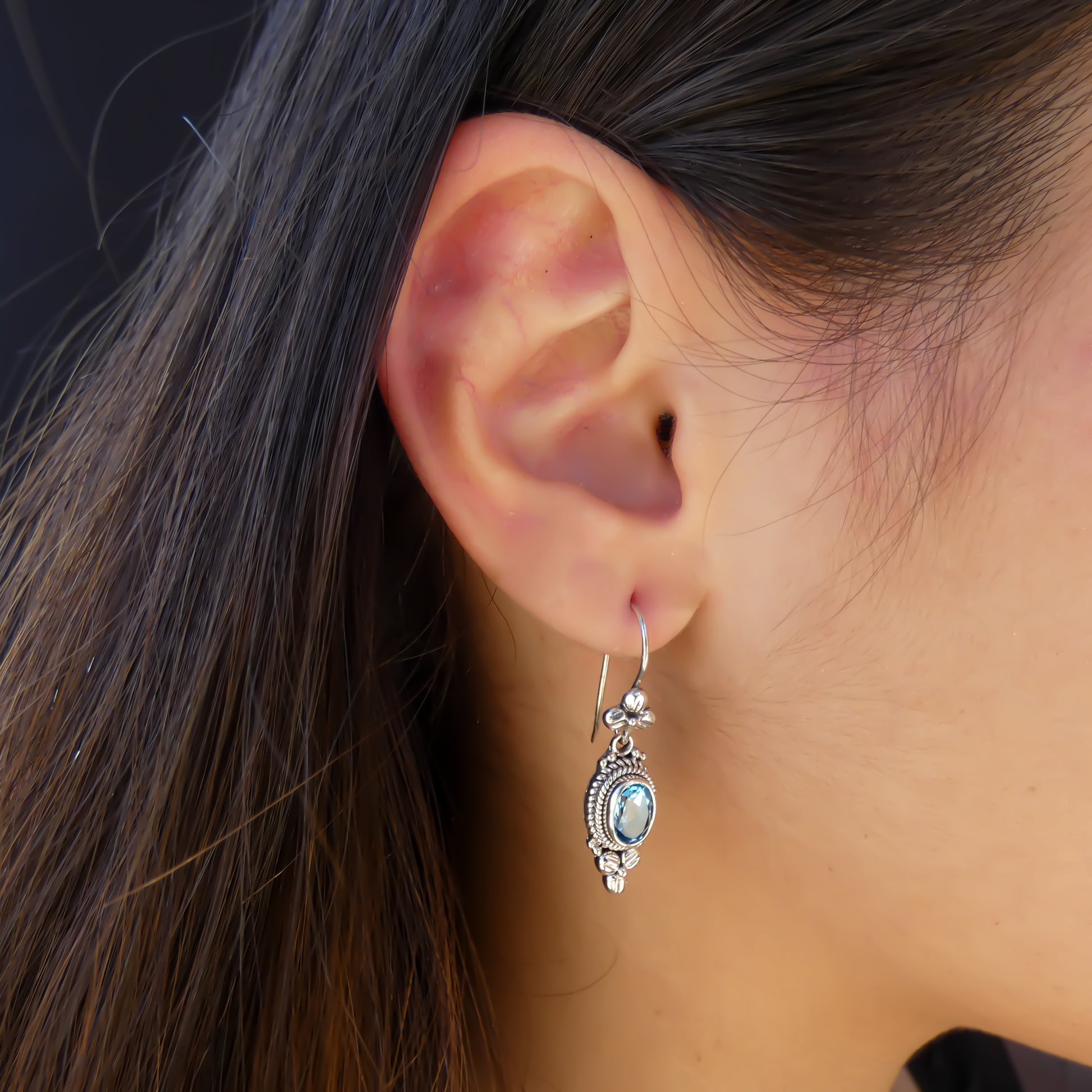 Woman wearing silver floral earrings with blue topaz stones.