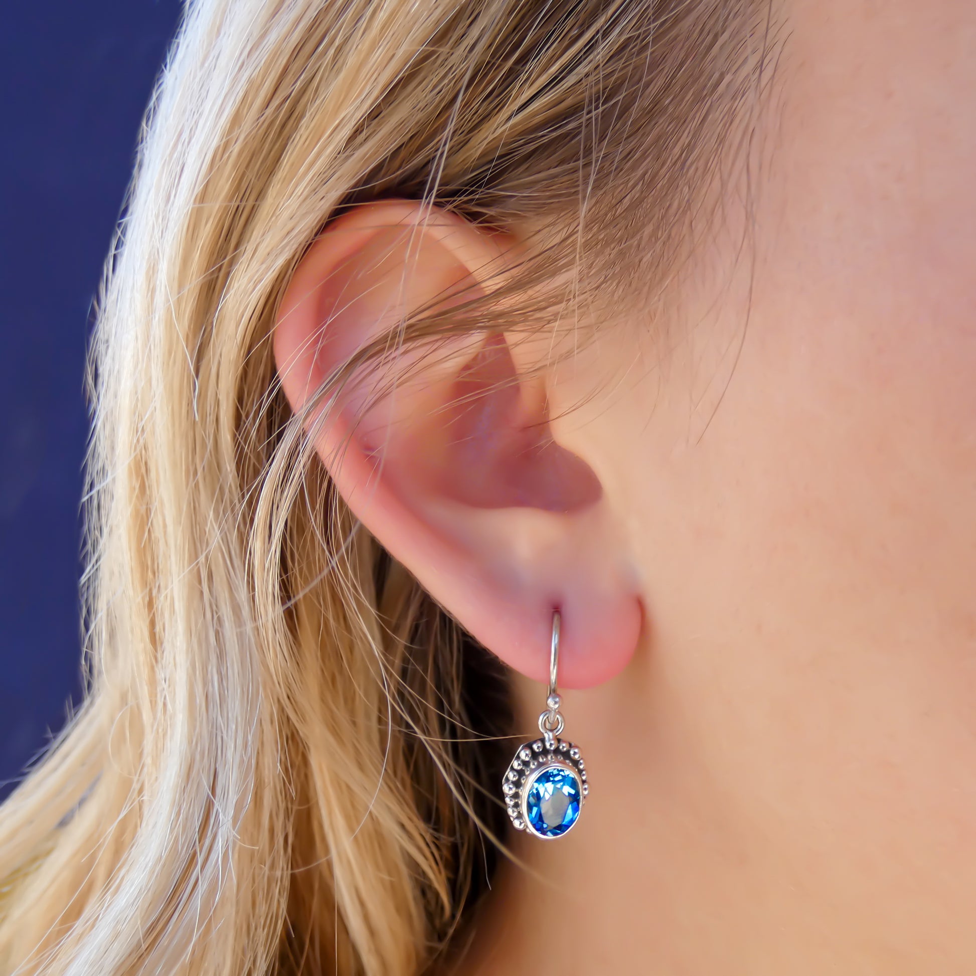 Woman wearing silver earrings with oval blue topaz gemstones.